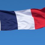 French flag blowing in the wind in a blue sky.